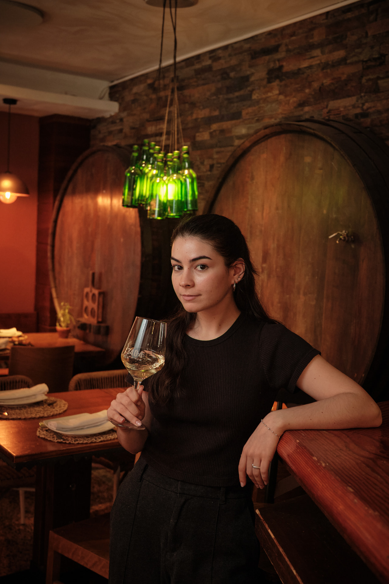 Mujer con una copa de vino blanco junto a grandes toneles de madera