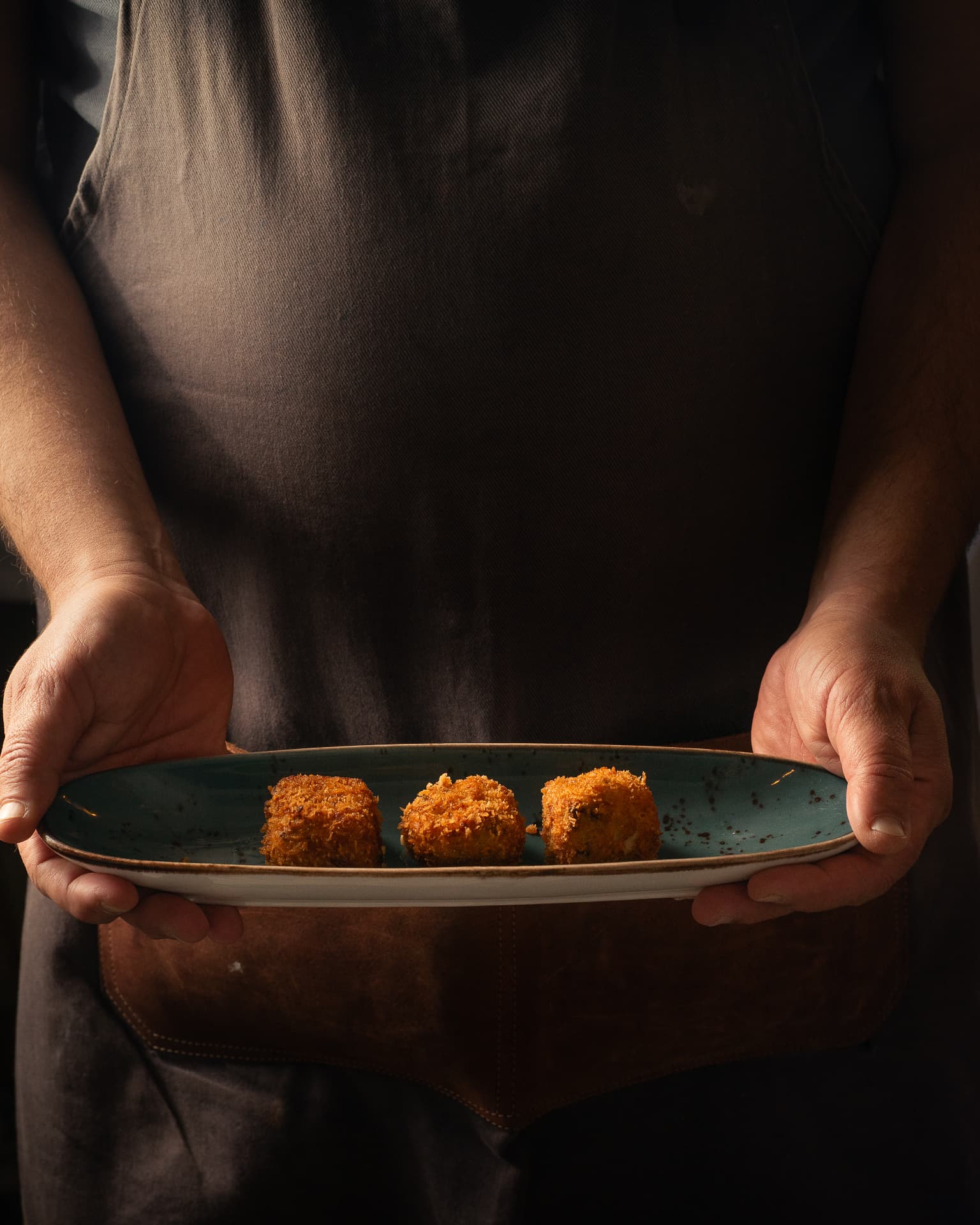 Cocinero sosteniendo un plato alargado con tres croquetas