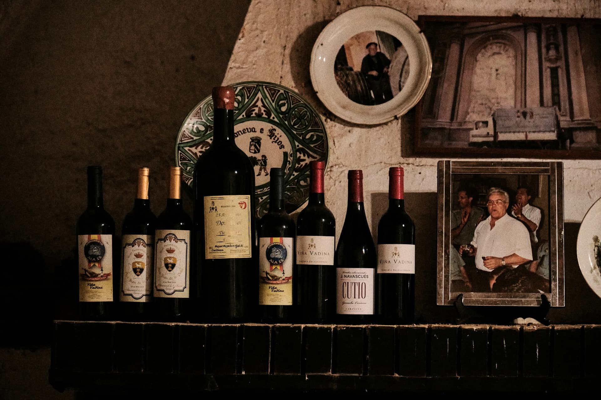 Botellas de vino alineadas sobre una repisa junto a fotografías antiguas