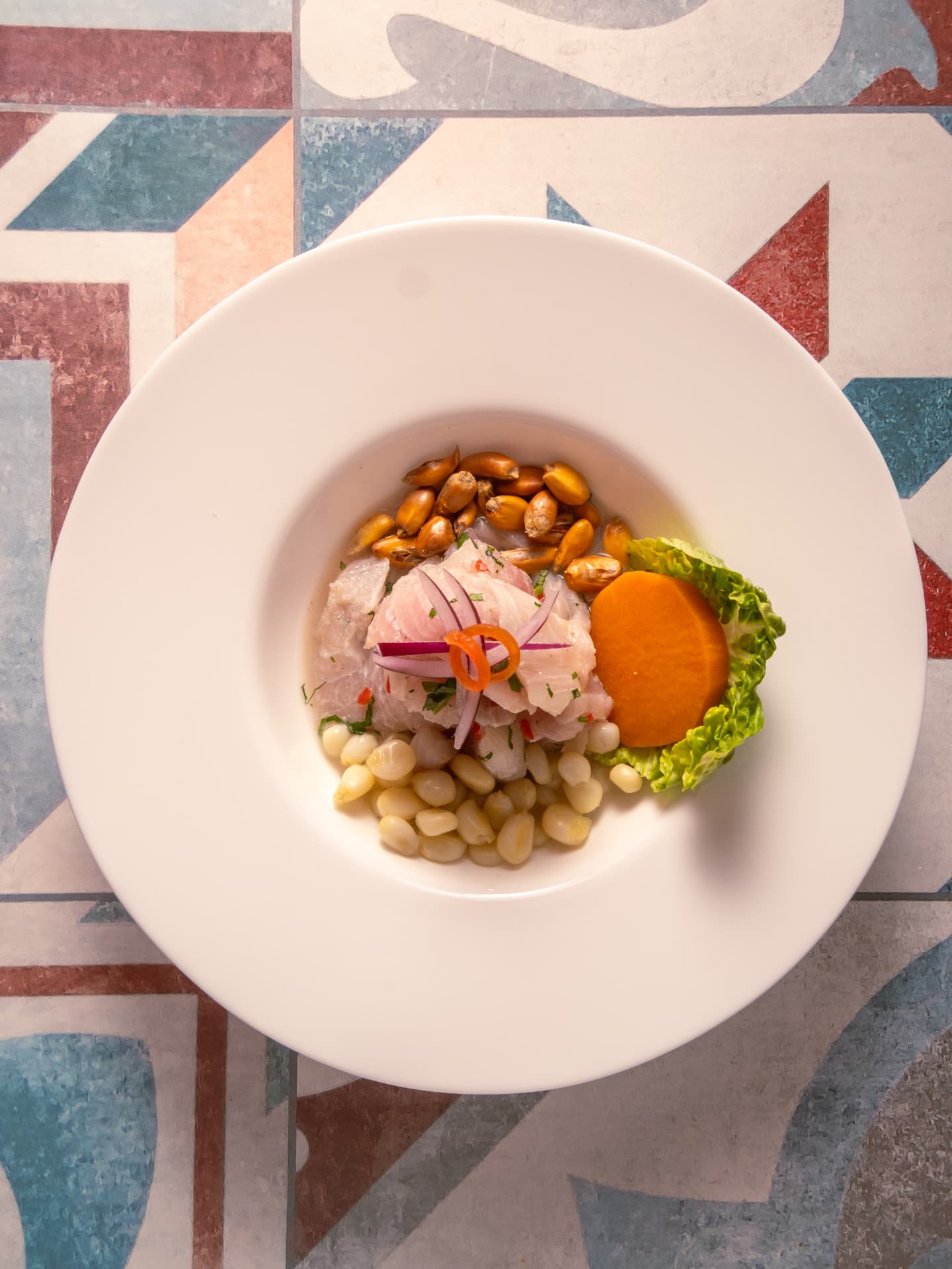 Plato de pescado marinado con maíz, boniato y lechuga sobre suelo de baldosas