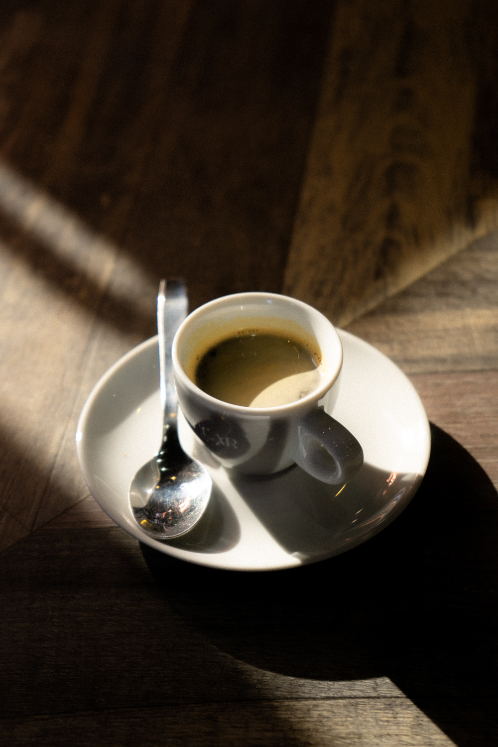 Taza de café solo con cucharilla sobre una mesa de madera iluminada por el sol