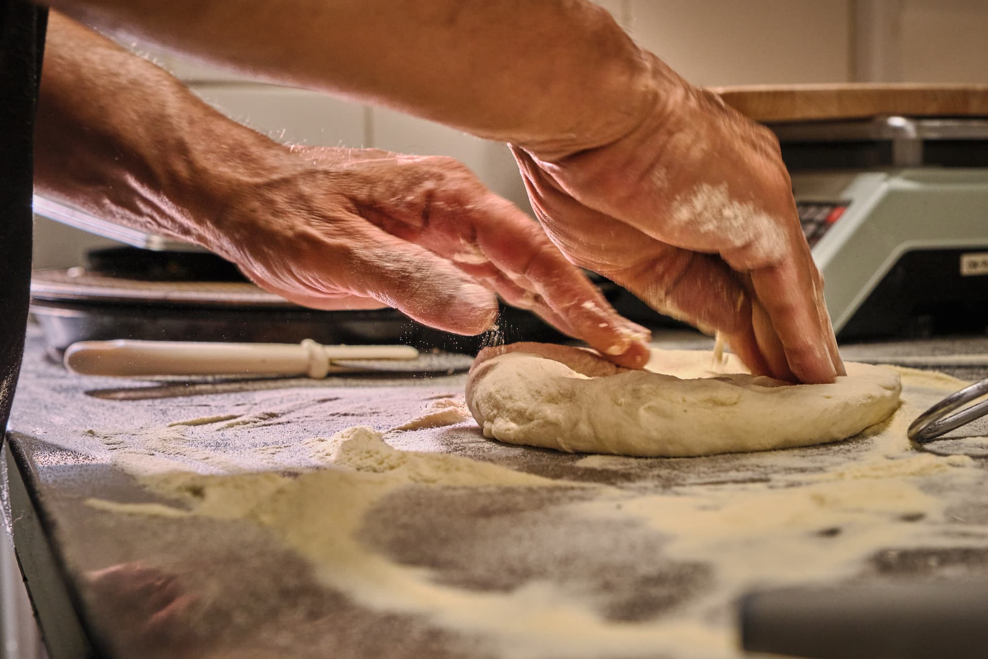 Manos amasando una base de masa sobre la mesa enharinada