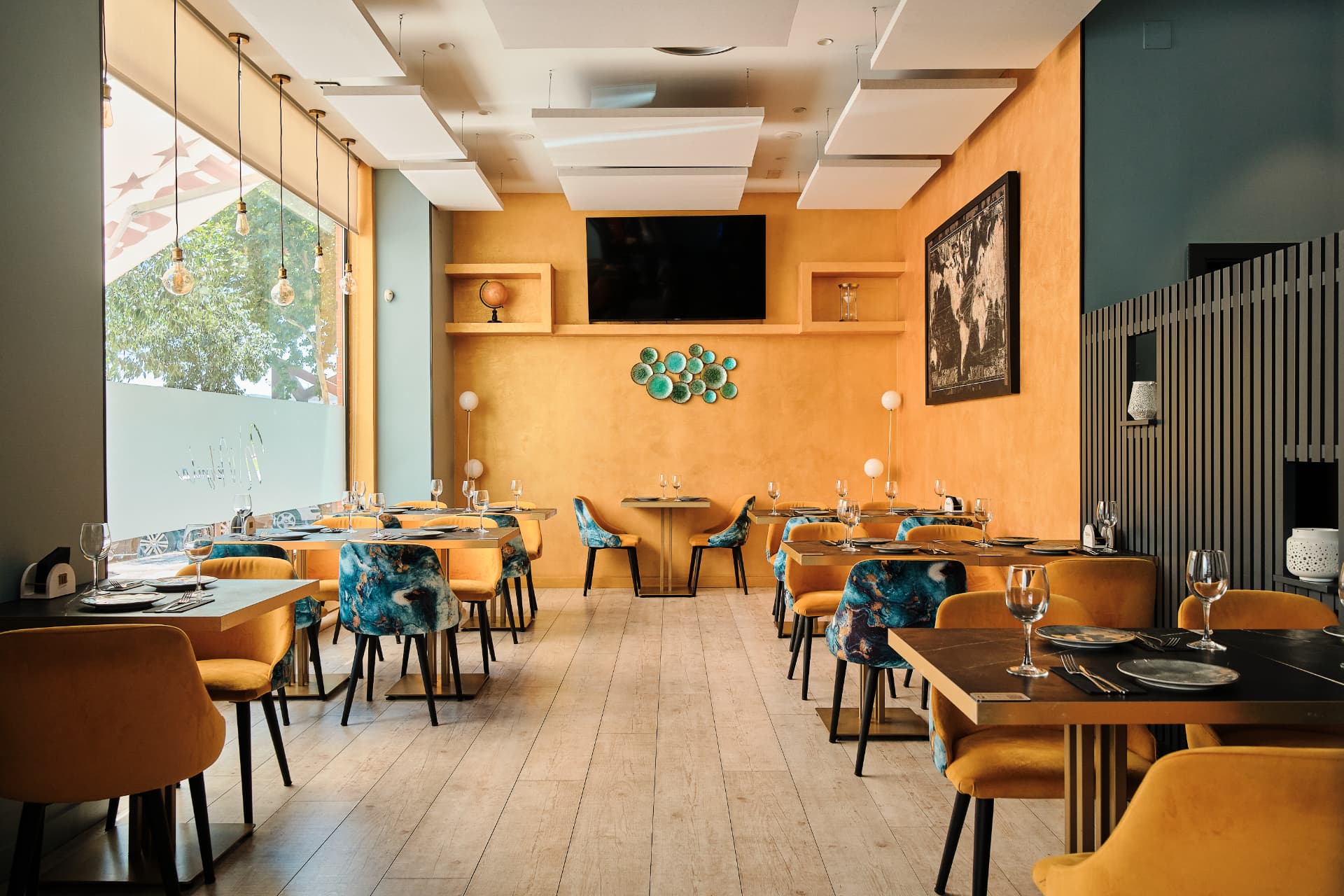 Comedor con mesas vestidas y sillas de terciopelo frente a una pared ocre