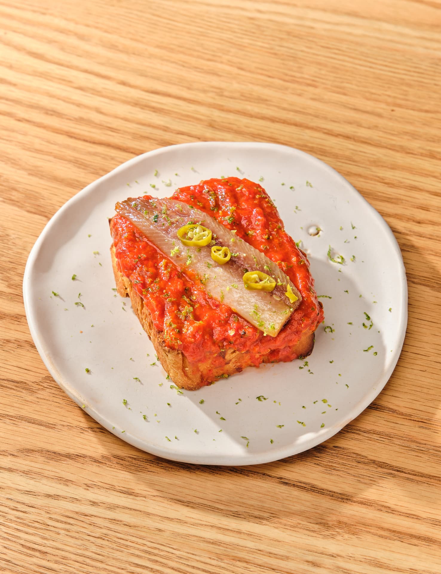 Tosta con salsa roja, pescado marinado y guindillas sobre un plato blanco
