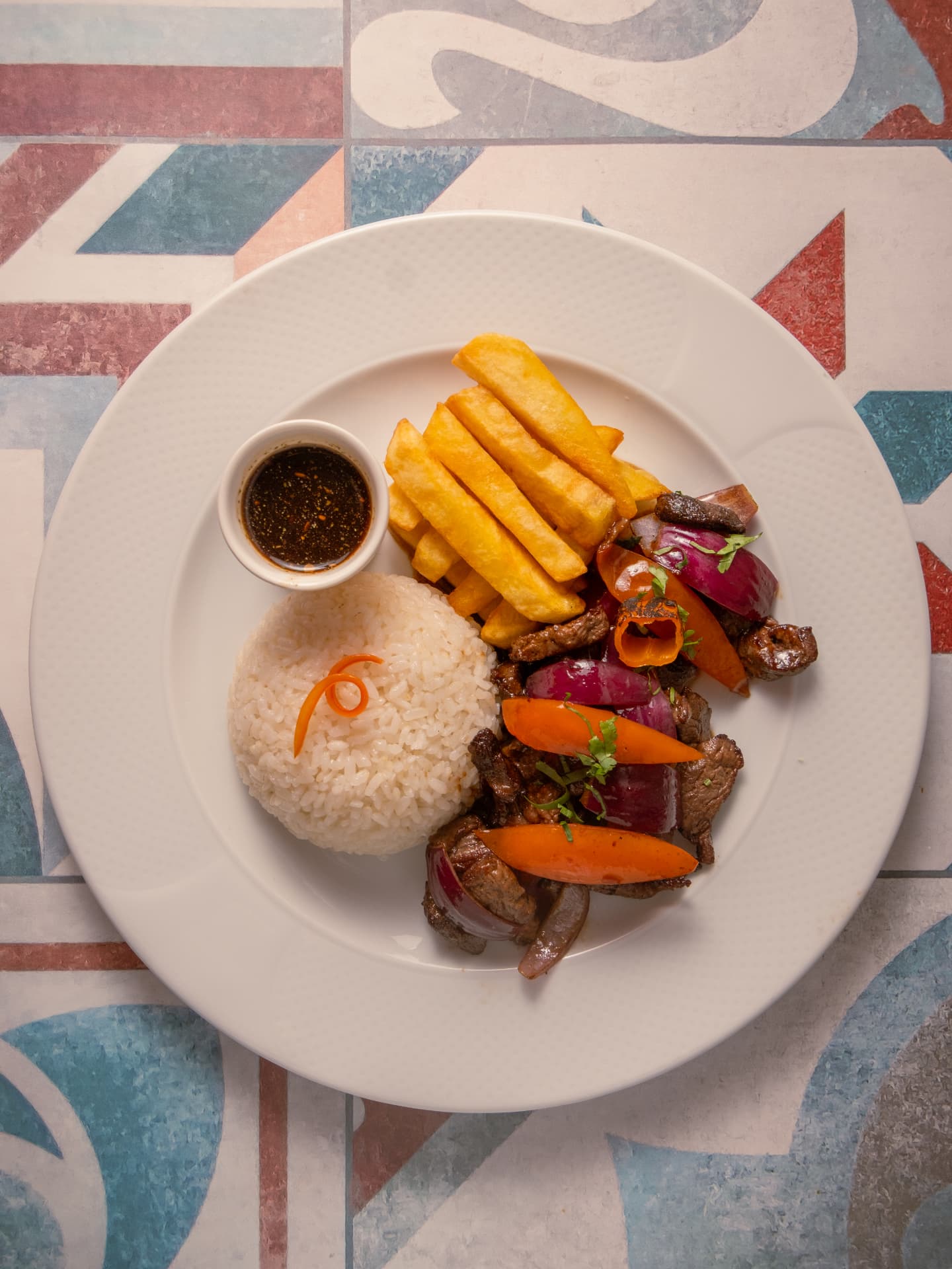 Plato de carne salteada con verduras, arroz y patatas fritas