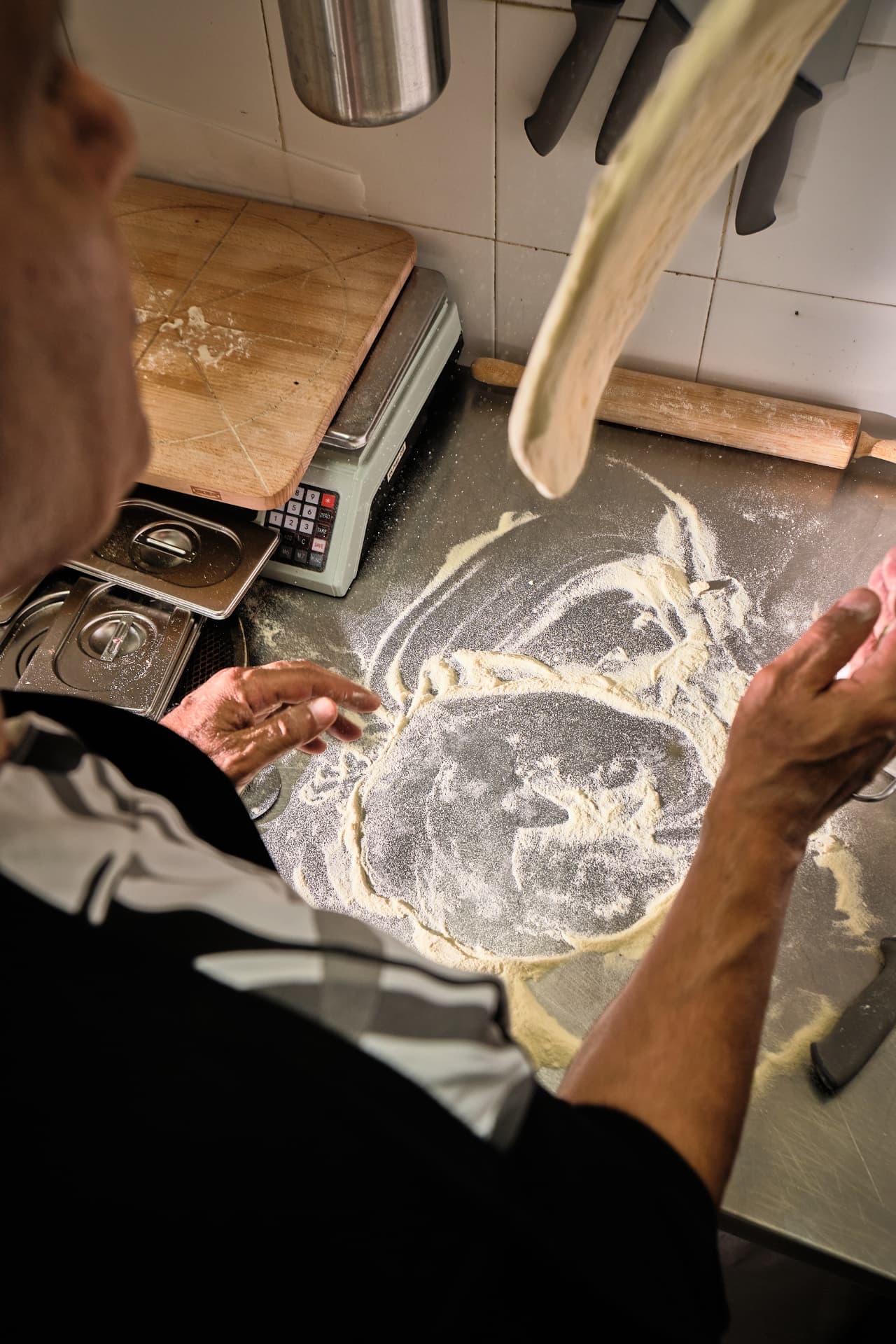 Cocinero estirando la masa en el aire sobre la mesa de trabajo