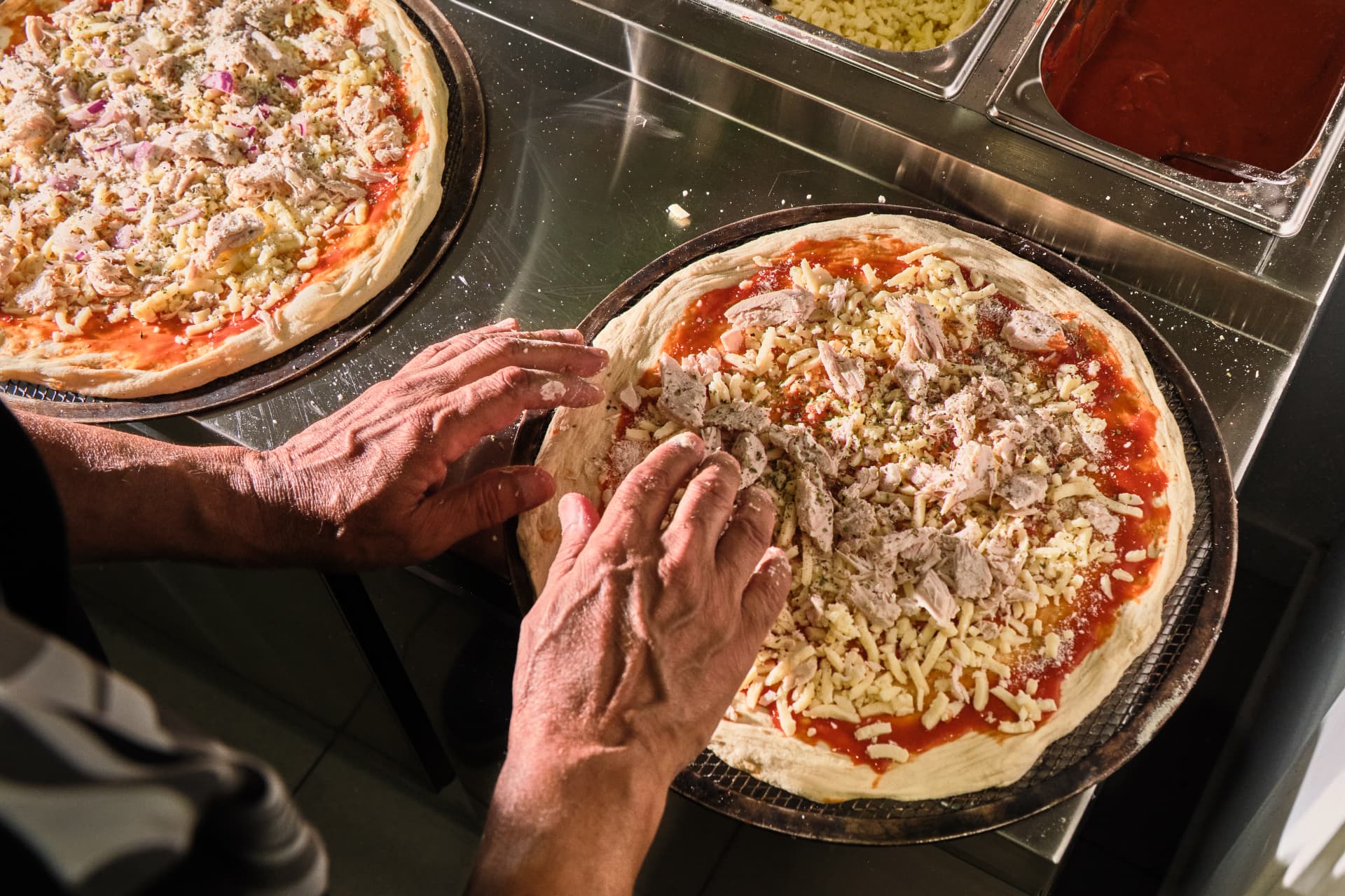 Manos añadiendo queso y pollo sobre dos bases de pizza