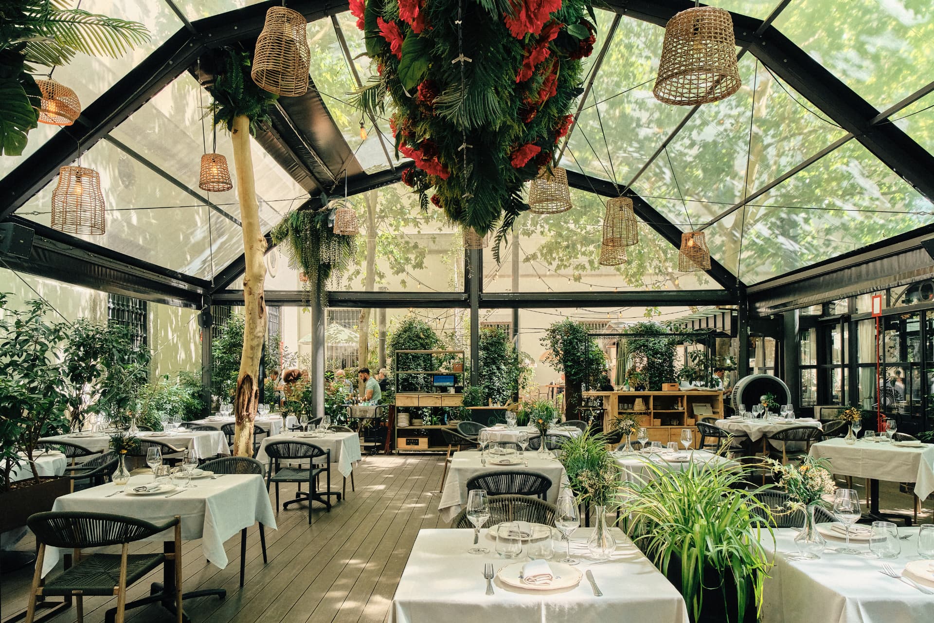 Sala acristalada con mesas vestidas de blanco y plantas colgantes