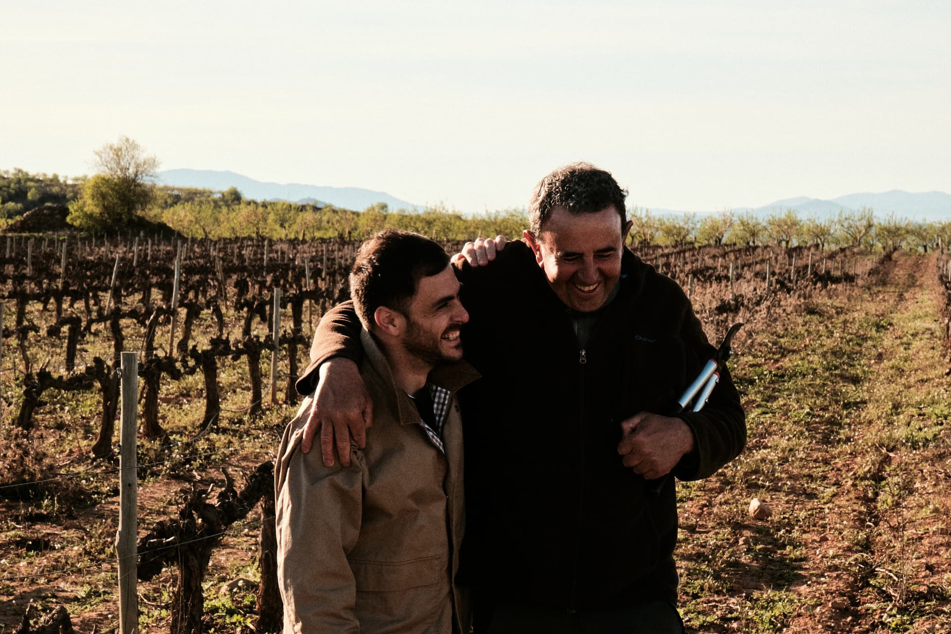 Dos hombres riendo abrazados en el viñedo