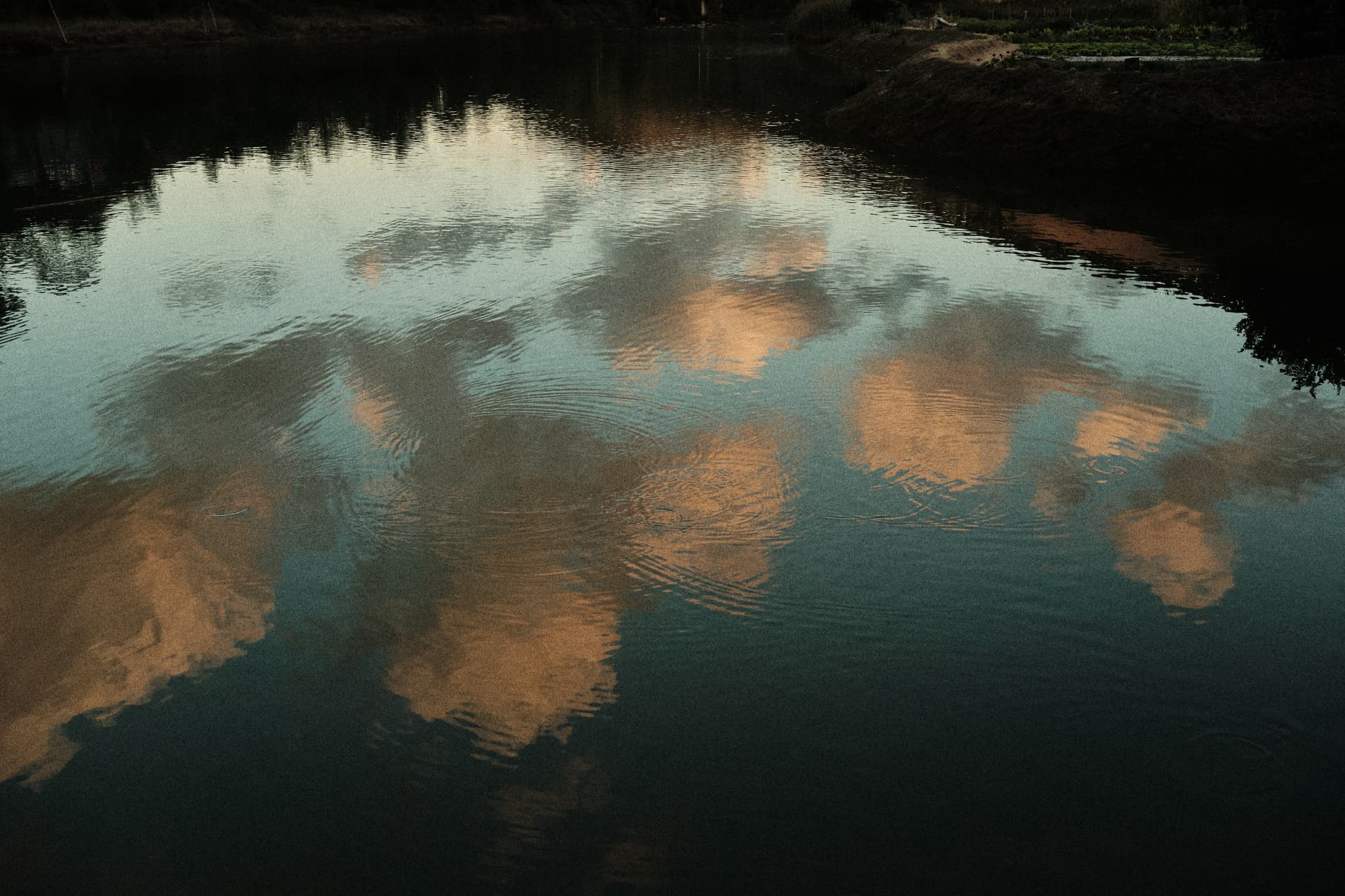 Agua oscura reflejando nubes y tonos cálidos